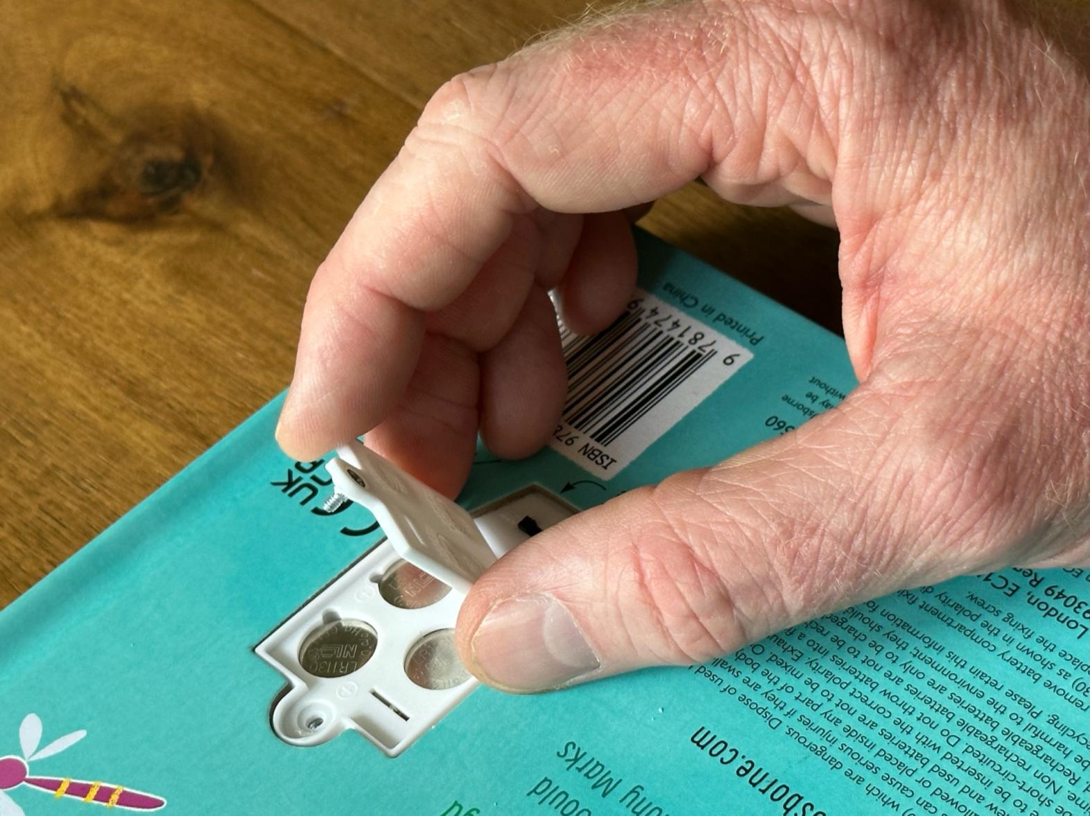 An adult removes the battery cover from a children's toy, exposing three button cell batteries