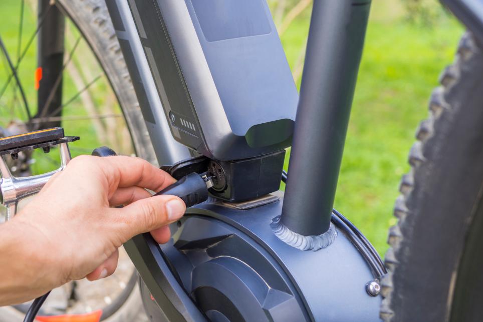 Masculine hand plugging a charger cord into an e-bike